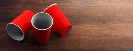 Plastic red color cups, disposable on wooden background, banner, copy space. 3d illustration
