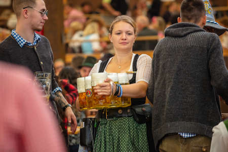 October 7, 2018. Munich, Germany, Oktoberfest, waitress in tyrolean costume holding beers, tent interior backgroundのeditorial素材