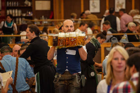 October 7, 2018. Munich, Germany, Oktoberfest, Waiter in tyrolean costume holding beers, tent interior backgroundのeditorial素材