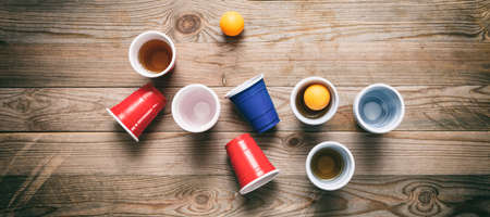 Beer pong, college party game. Plastic red and blue color cups and ping pong balls on wooden background, top view, bannerの写真素材