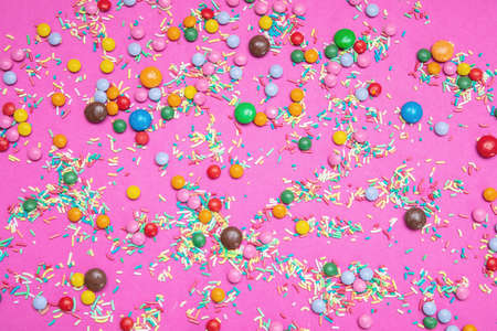 Birthday concept. Colorful sprinkles and candies on bright pink background, top view