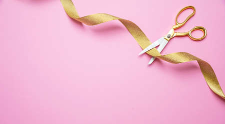 Grand opening concept. Gold scissors cutting golden ribbon against pink background, copy space, top view.の写真素材