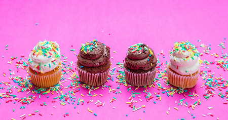 Cupcakes on bright pink background. Four cupcakes vanilla and chocolate with colorful sprinkles, closeup viewの写真素材
