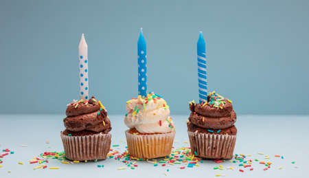 Birthday cupcakes on blue pastel background. Three cupcakes vanilla and chocolate with blue candlesの写真素材
