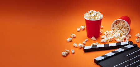 Cinema film concept. Fresh salty pop corn and movie clapper board, orange color background, bannerの写真素材