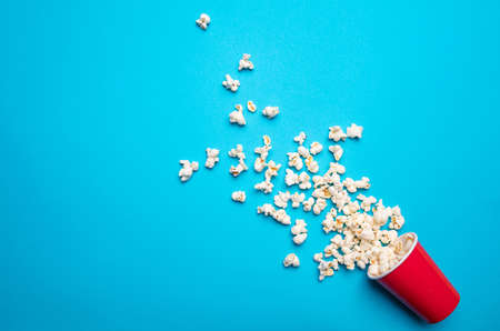 Fresh salty pop corn spilled out of a red carton container, blue color background, copy space