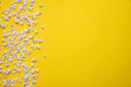 Fresh salty pop corn scattered on yellow color background, copy space, top view