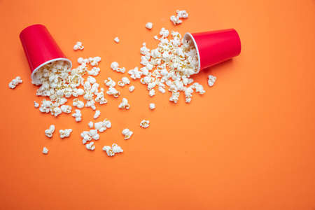 Fresh salty pop corn spilled out of two red carton containers, orange color background, copy space