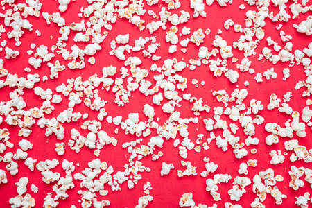 Fresh salty pop corn scattered on red color background, full frame, top view