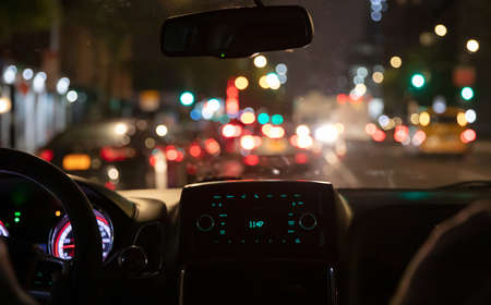 Driving in New York at night. Interior view of taxi cab in traffic. Close up view on the dashboard. Colorful bokeh lights out of the windowの写真素材