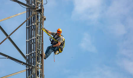 Canton, Ohio lake, USA. May 8, 2019. Communication maintenance. Technician climbing on telecom tower antenna against blue sky background, copy spaceのeditorial素材
