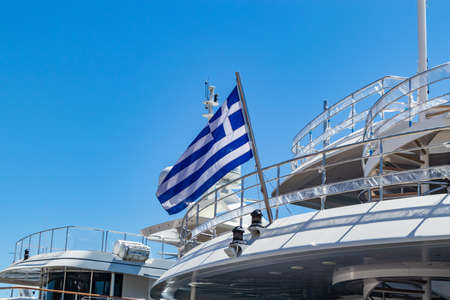Greek flag on luxury yacht stern. Ongoing cruise to Greece. Clear blue sky background, close up view.の写真素材