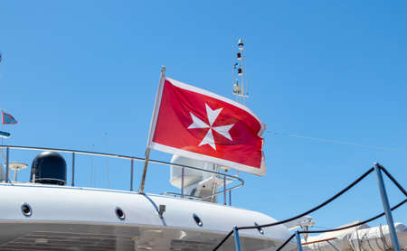 Maltese old flag and small greek flag on yacht stern. Boat at marina Zeas, Greece. Blue sky...