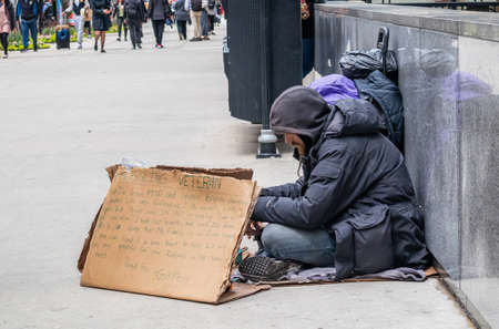 USA, Chicago, Illinois. May 9, 2019. Homeless veteran sitting on the roadside holding a cardboard sign, asking for help, downtownのeditorial素材