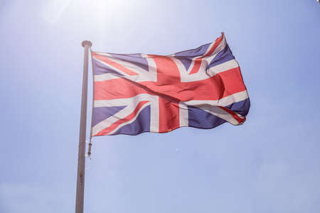 United Kingdom flag, Great Britain national symbol waving against clear blue sky, sunny dayの写真素材