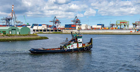 Tug boat, containers and huge cranes at international harbor of Rotterdam, Netherlands, sunny day. Logistics business.の写真素材