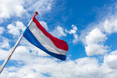 Netherlands flag. Dutch national symbol waving on liberation day against blue sky with clouds, sunny day, copy spaceの写真素材