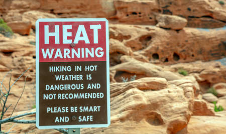 Heat warning sign in Valley of fire state park, Nevada USA. Red sandstone formations background, sunny spring day.の写真素材