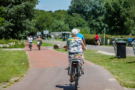 Rotterdam, Netherlands. June 30, 2019. Mature woman riding bicycle in a park, back view, Spring sunny dayのeditorial素材