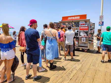 Santa Monica. California, USA. May 30, 2019. Japadog Street food, People queue wait, on wooden pier in front of traditional shop for famous hotdog. Sea and blue sky background.のeditorial素材