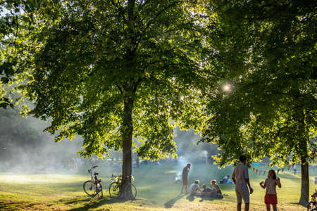 Rotterdam, Netherlands. June 29, 2019. Picnic on the grass, people relaxing, sun behind the trees foliage, summer afternoon in a city parkのeditorial素材