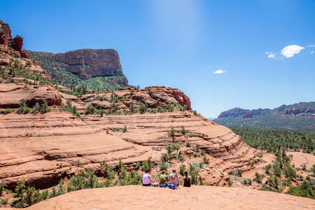 Sedona Arizona USA. May 25, 2019. Group of young hikers sitting on terrain looking at the view. Red orange desert  landscape, clear blue sky, sunny spring dayのeditorial素材