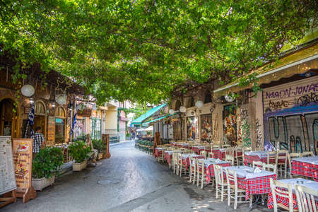 Athens, Greece - August 4, 2019: Plaka, narrow street with lush greenery and outside greek tavern tables in historical centerのeditorial素材