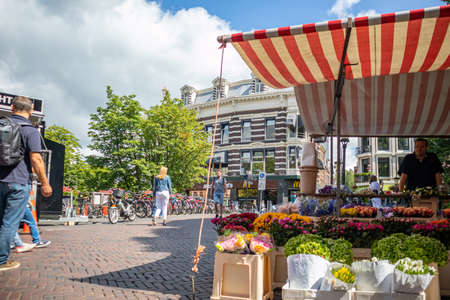 Utrecht, Netherlands - JULY 01, 2019: People walking on paved city street by parked bicycles for rent and flower market with striped canopyのeditorial素材