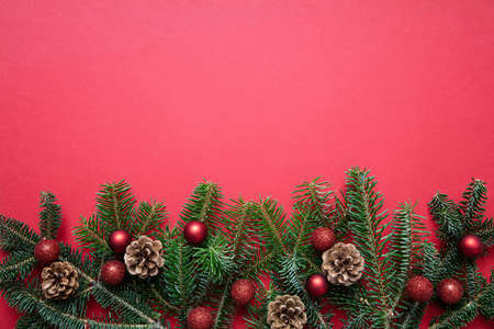 Christmas decoration. Fir tree twig fresh and pine cones against red color background, top view, copy spaceの写真素材