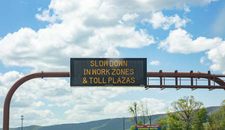 Pennsylvania highway, USA. May 6, 2019: Slow down in work zones and toll plazas Warning led road sign billboard on a highway, cloudy blue skyのeditorial素材