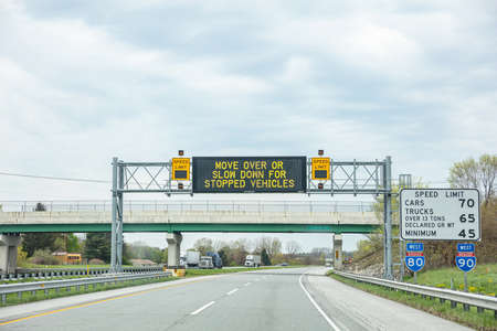 Illinois highway, USA. May 8, 2019: Warning road sign billboard for stopped vehicles and speed limits on a highway, cloudy skyのeditorial素材