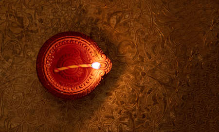 Diwali, Hindu festival of lights. Clay diya candle illuminated in Dipavali. Oil lamp on traditional tray, copy space.の写真素材