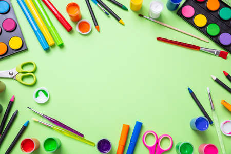 Kids creativity. Colorful paints and paintbrushes flat lay on pastel green color background, top...