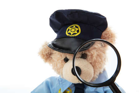 Police officer teddy bear in uniform and a magnifying glass isolated against white backgroundの写真素材