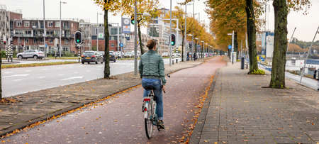 Rotterdam Netherlands, October 13, 2019. Rear view of a woman riding a bike, urban background, cloudy autumn dayのeditorial素材