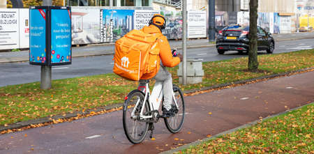 Rotterdam Netherlands, October 13, 2019. Food delivery. Rear view of a man riding a bike, urban background, autumn dayのeditorial素材