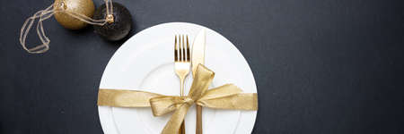 Christmas table setting. Gold cutlery and white set of dishes against black background, banner, top viewの写真素材