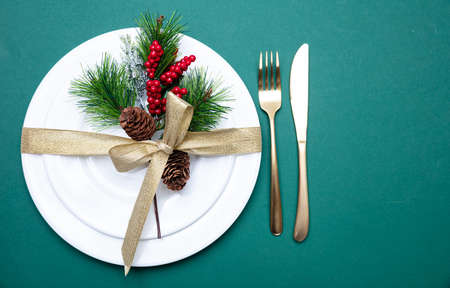 Christmas table setting. Gold cutlery and white set of dishes against green background, top view