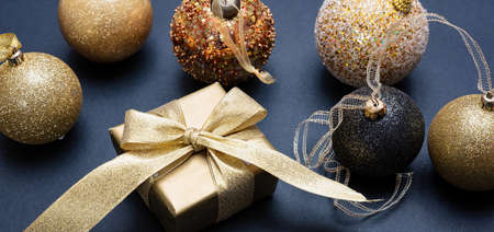 Christmas decoration. Xmas balls and gift box shiny gold color against dark gray background, high...