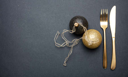Christmas table setting. Gold cutlery and christmas balls against black background, top view