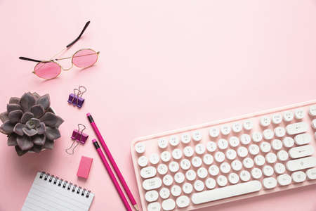 Woman office desk. Computer keyboard and notepad against pink background, copy spaceの写真素材