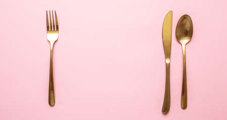 Gold and pink luxury table setting. Golden cutlery set against pink background. Top view, copy spaceの写真素材