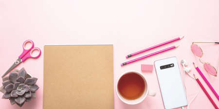 Creative woman office desk. Kraft paper notepad, mobile phone and tea cup against pink background, copy spaceの写真素材