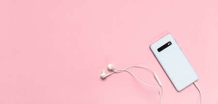 Mobile phone back view white color and earphones against pink color background, banner, copy spaceの写真素材