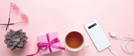 Women day gift, office desk. Gift box, mobile phone and tea cup against pink background, copy spaceの写真素材