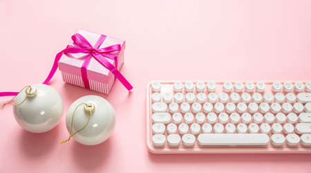 Christmas office in pink color. Xmas balls, gift and computer keyboard against pink background, top...
