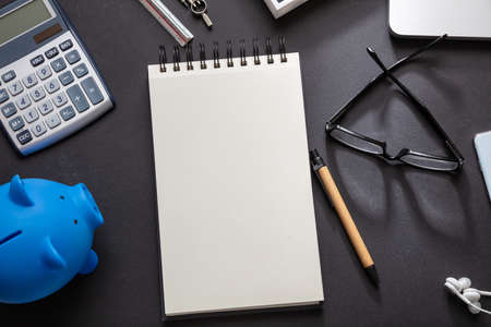 Construction cost estimation concept. Blue piggy bank, calculator and blank notepad on black...