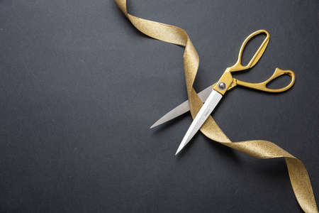 Grand opening. Gold scissors cutting gold silk ribbon, black background, top view, copy spaceの写真素材