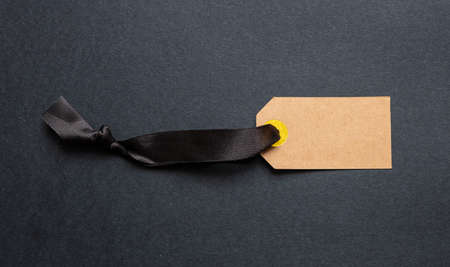 Black Friday sale concept. Kraft recycled price tag blank mockup with satin ribbon isolated against black background, copy spaceの写真素材