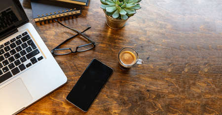 Office desk, cozy warm workspace. Computer laptop and mobile phone on a chestnut wood table, copy...